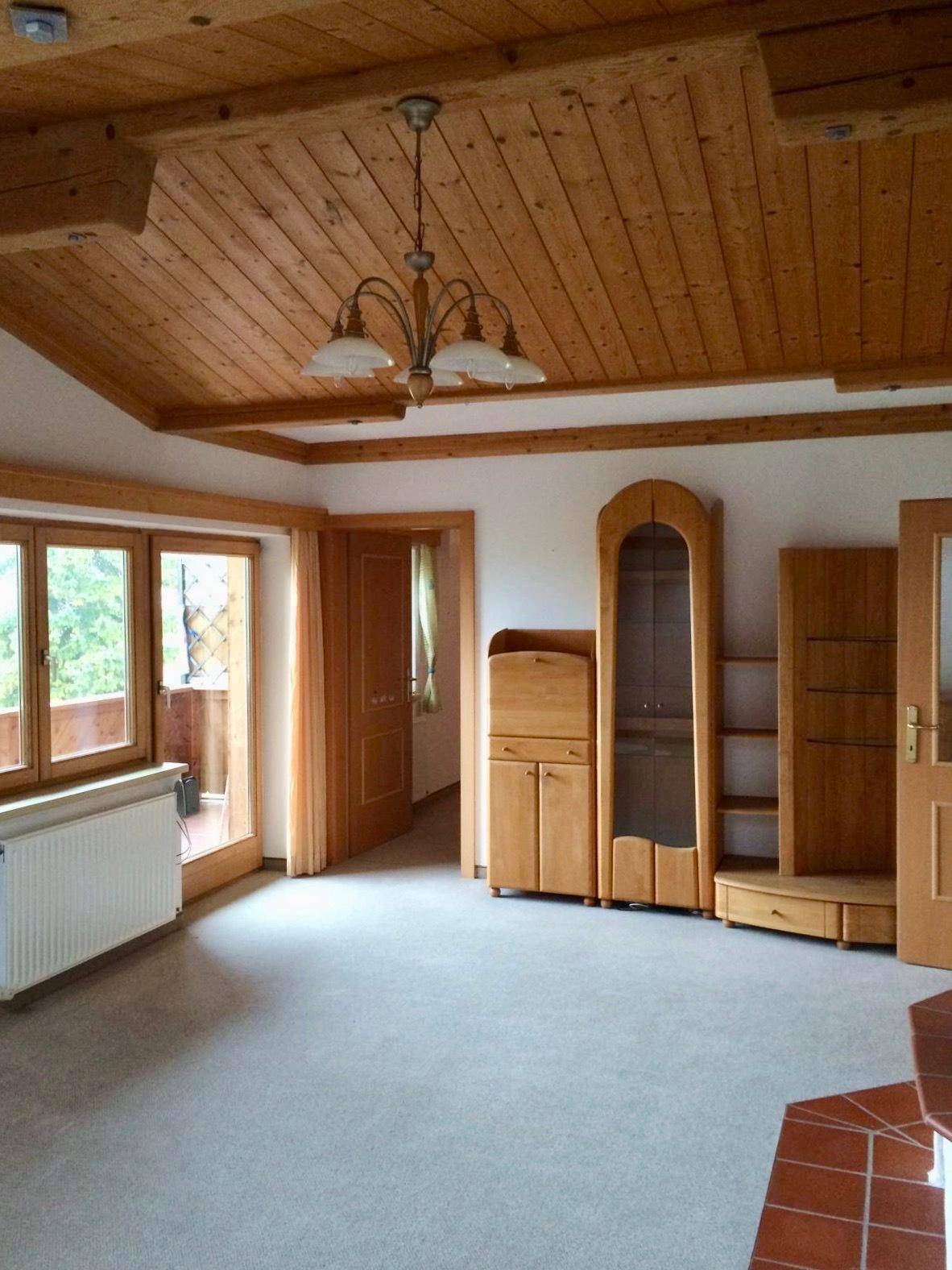 Wohnzimmer mit traditioneller Holzbalkendecke, Teppichboden und Zugang zum Balkon.