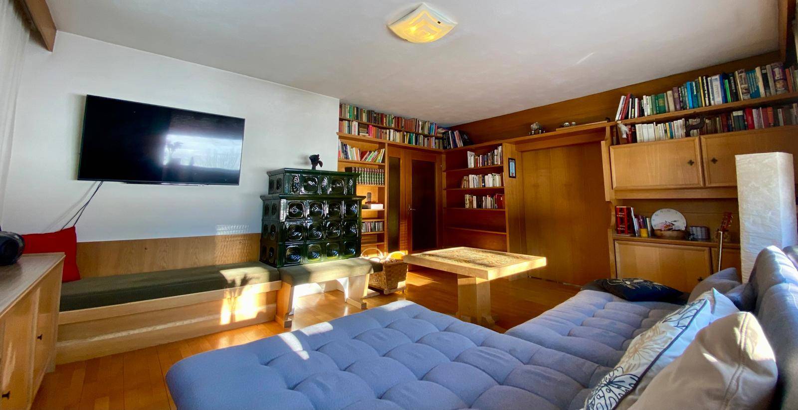 Gemütliches Wohnzimmer mit traditionellem Kachelofen, Bücherregalen und Holzboden.