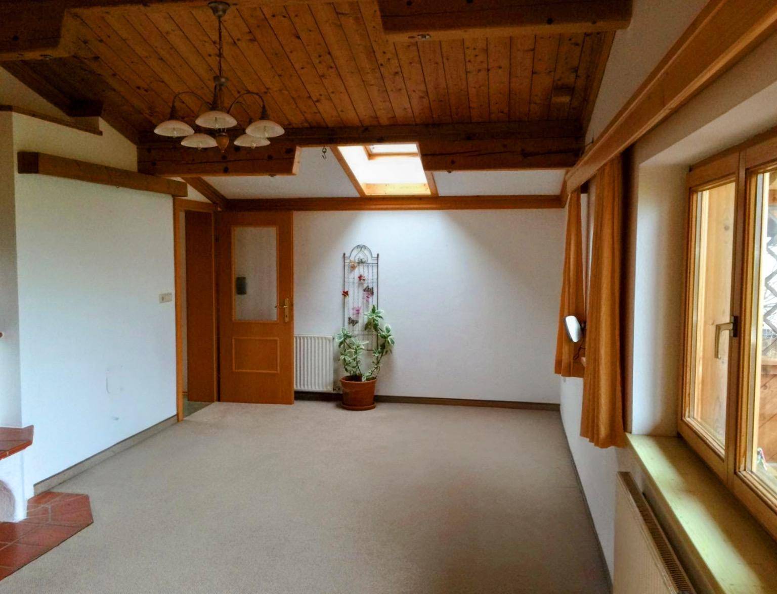 Geräumiges Wohnzimmer mit Holzbalkendecke, Teppichboden und Dachfenster für Tageslicht.