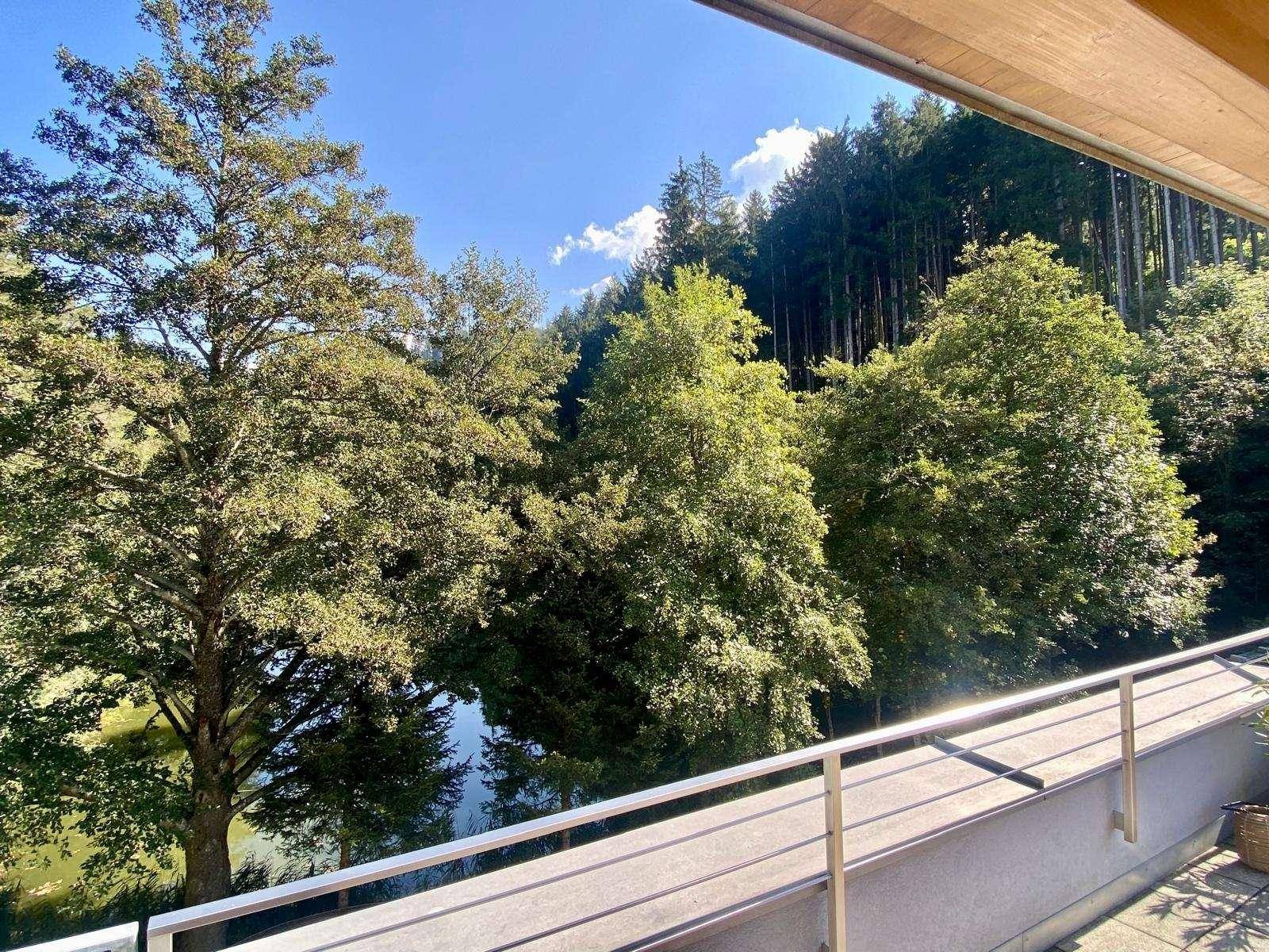 Balkon mit Metallgeländer und weitem Blick auf den See und die umliegenden Wälder.