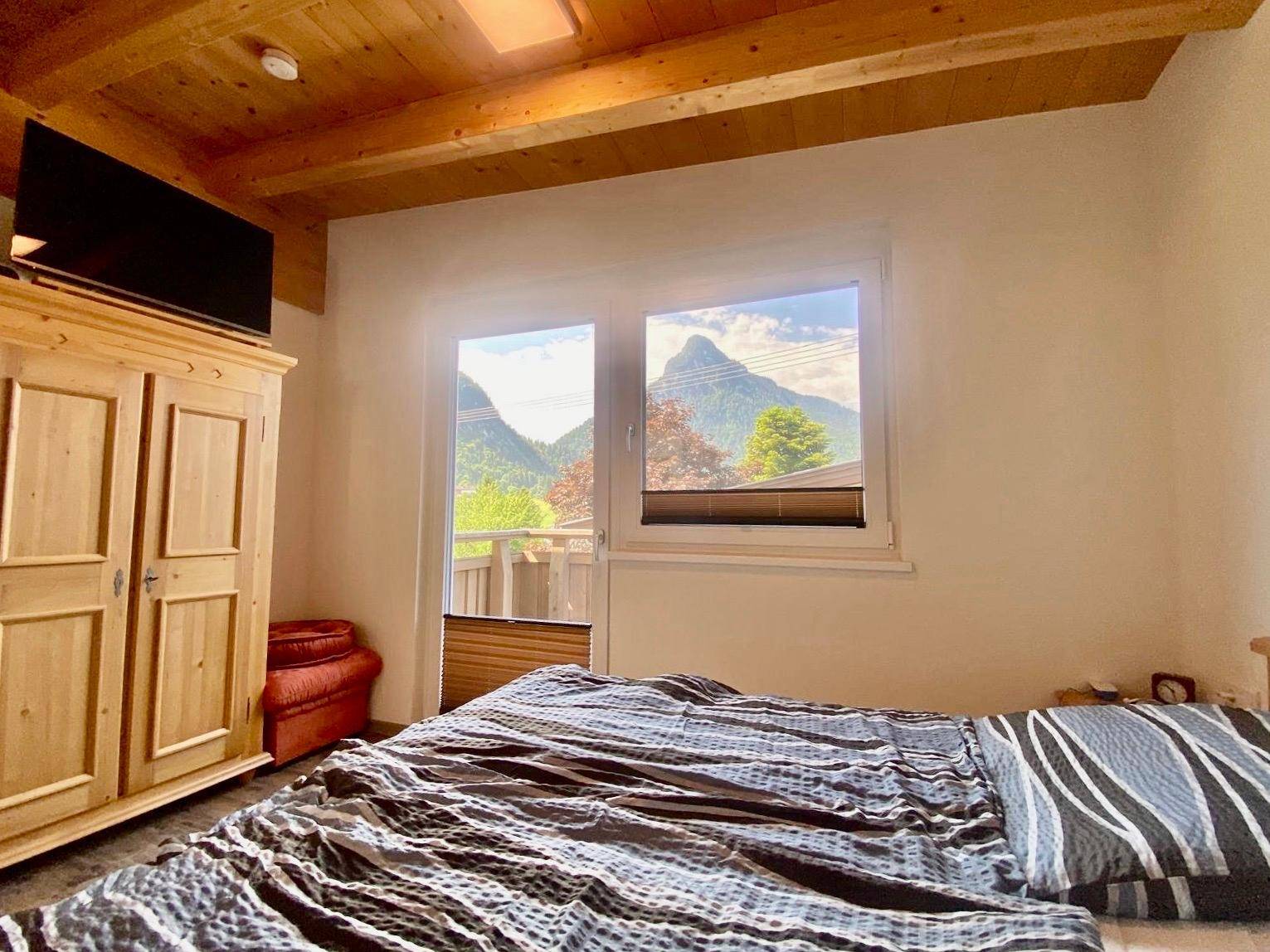 Schlafzimmer mit Holzkleiderschrank, Holzbalkendecke und Bergblick durch das Fenster.
