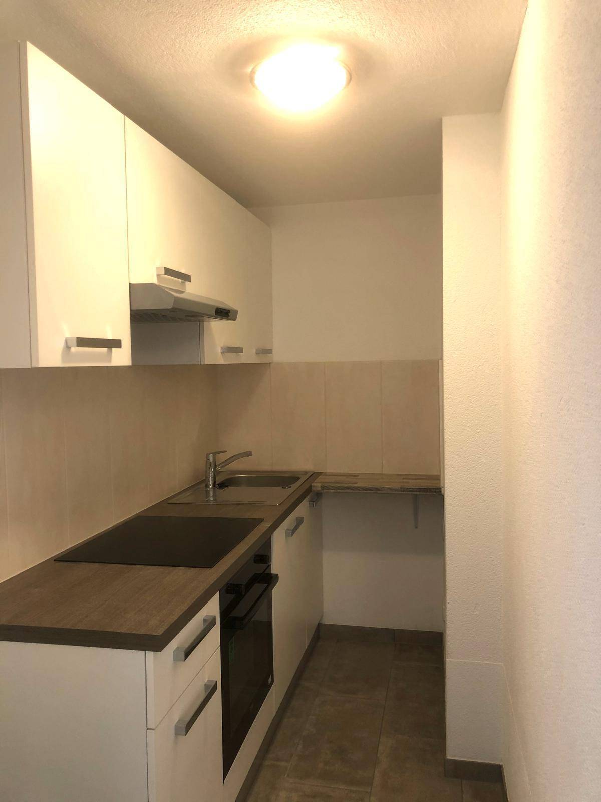 Kompakte Küchenzeile mit weißen Schränken, Spüle, Induktionskochfeld und integriertem Backofen.