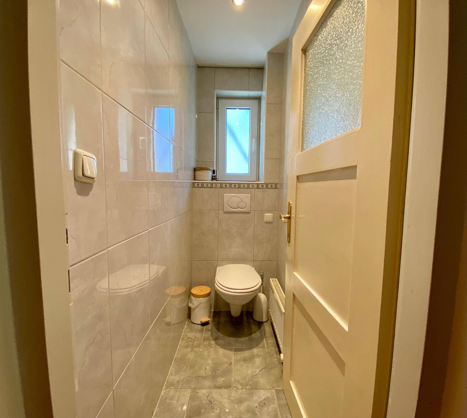 Separate Toilette mit Fenster und hellen Fliesen, funktional eingerichtet.