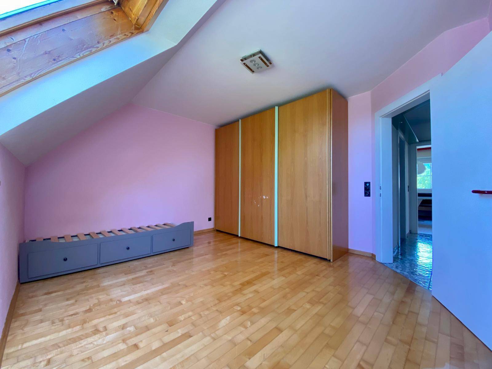 Schlafzimmer mit Dachschräge, Holzfußboden, Bettrahmen und einem großen Holzschrank.