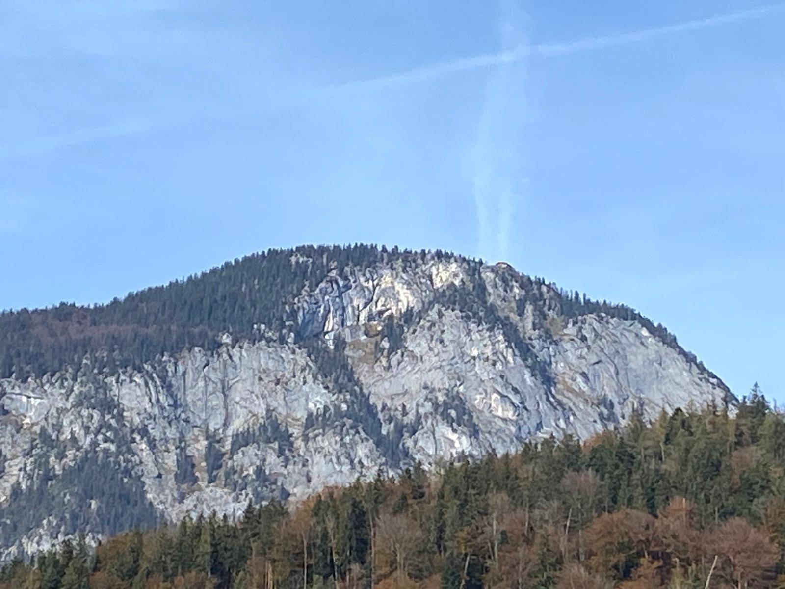 Detailaufnahme der felsigen Berglandschaft mit bewaldeten Hängen unter einem strahlend blauen Himmel.