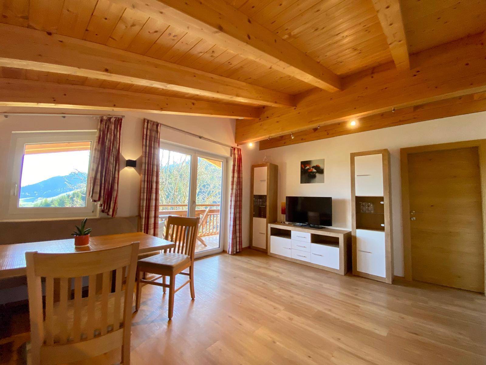 Heller Wohn- und Essbereich mit Holzbalkendecke, Parkettboden und Zugang zum Balkon.