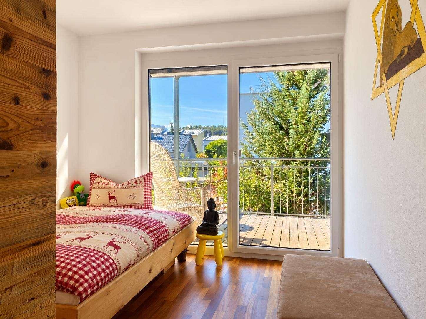 Helles Kinderzimmer mit Holzboden, Einzelbett und Zugang zu einem sonnigen Balkon mit Weitblick.