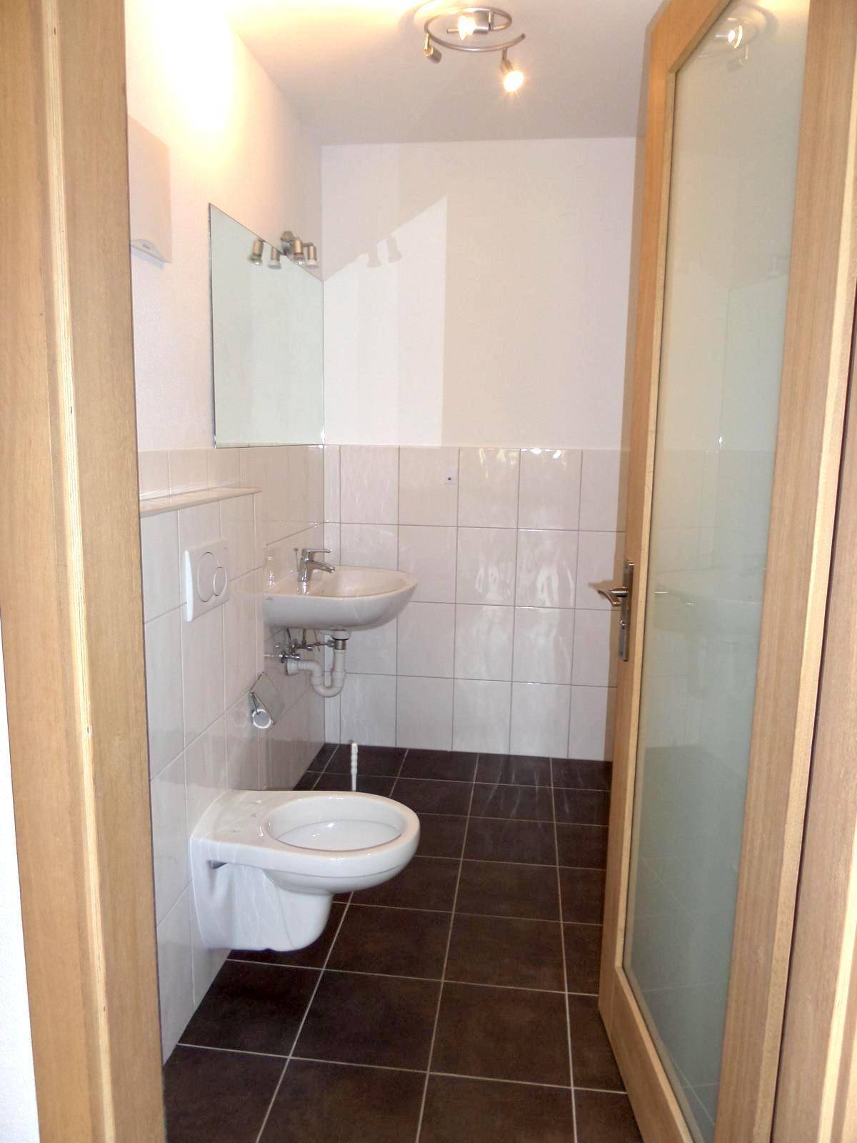 Kleines Gäste-WC mit Waschbecken, Wand-WC und dunklen Bodenfliesen.