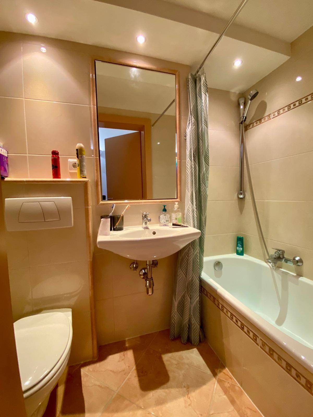Badezimmer mit Badewanne, WC und Waschbecken, komplett gefliest in warmen Farbtönen.