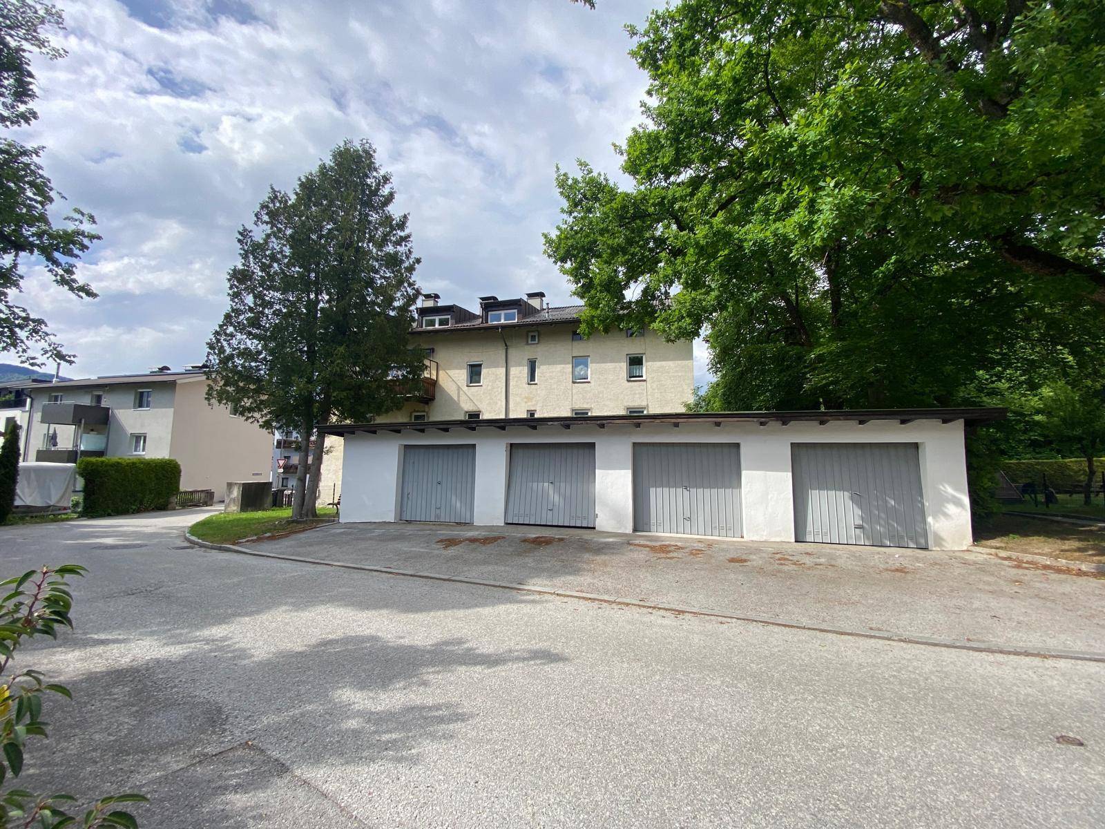 Reihe von Garagenboxen mit grauen Toren vor einem mehrstöckigen Wohngebäude mit Bäumen.
