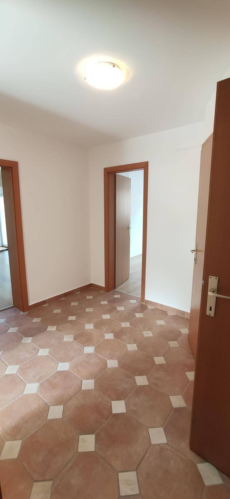 Heller Flur mit Terrakotta-Fliesenboden und mehreren Holztüren, der verschiedene Räume verbindet.