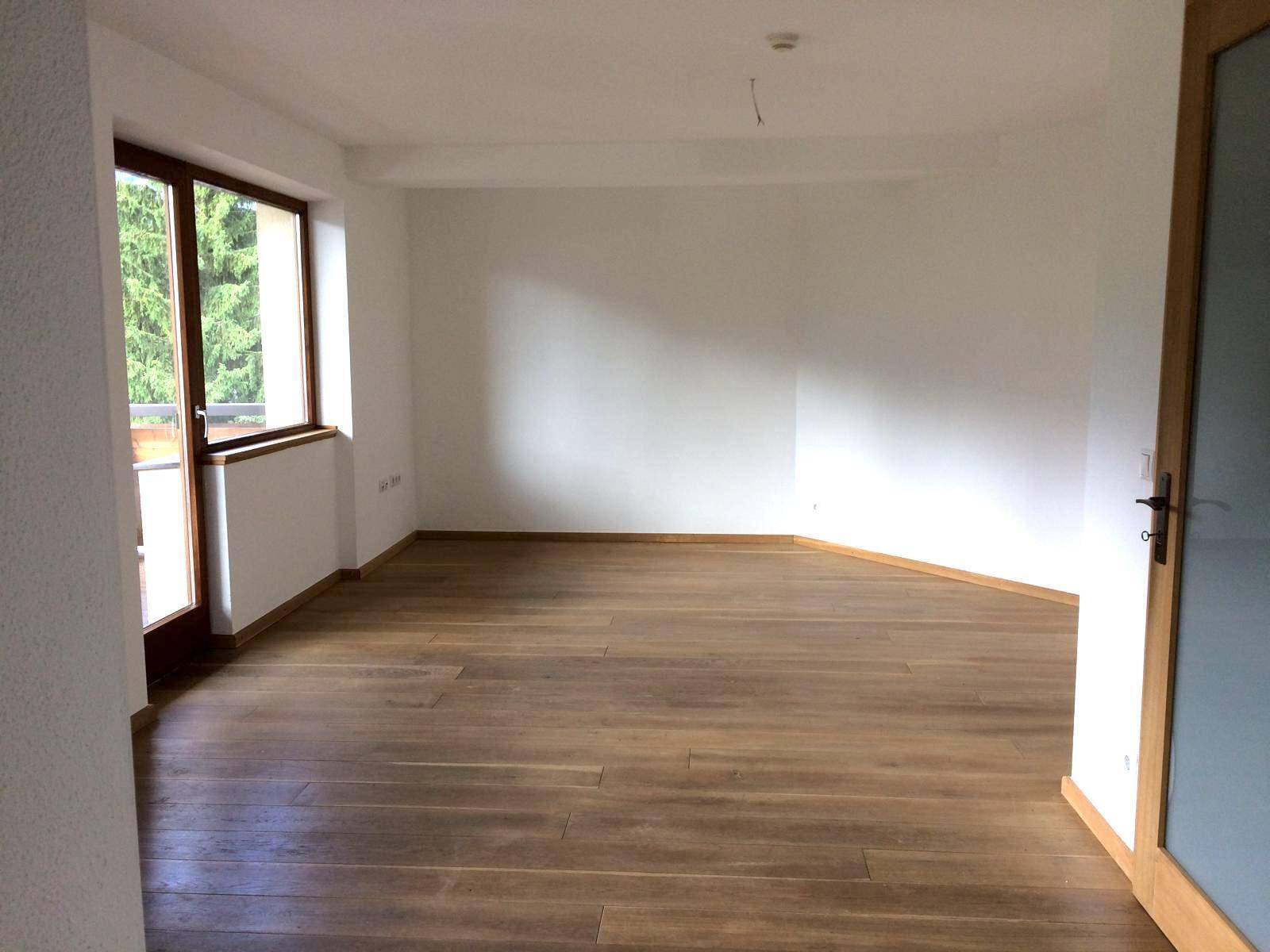 Helles, leeres Zimmer mit Holzboden und großen Fenstern, bereit zur individuellen Gestaltung.