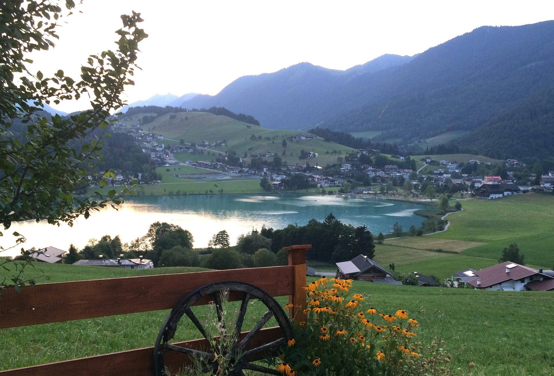 Idyllischer Blick auf den See und das Dorf, umgeben von grünen Hügeln und Bergen.