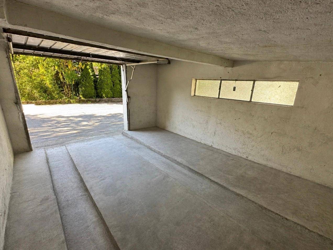 Leere Garagenbox mit Betonboden und einem kleinen Fenster, das Tageslicht hereinlässt.