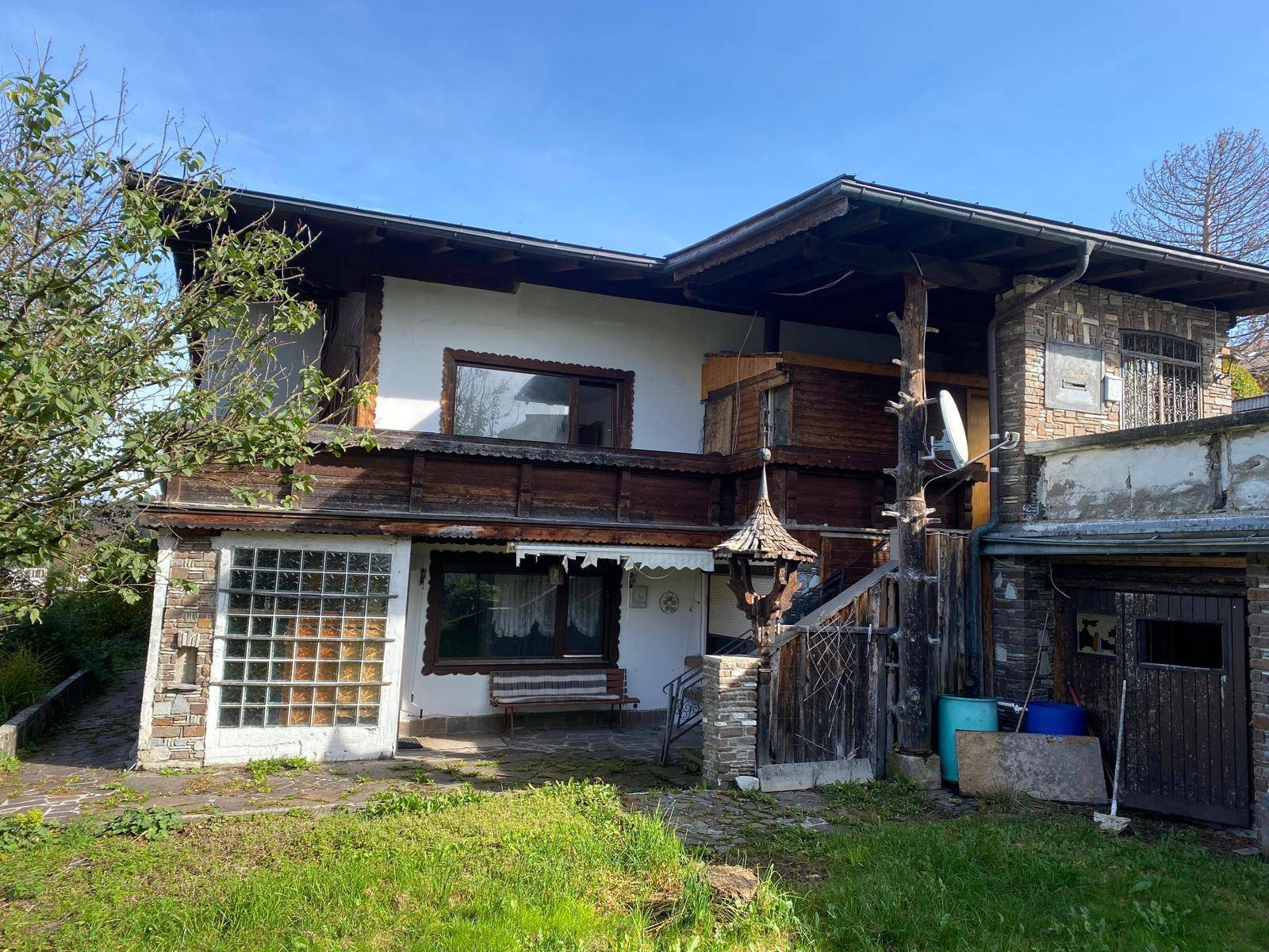 Vorderansicht des Hauses mit traditionellen Holzelementen und Fenstern, umgeben von Grünflächen.
