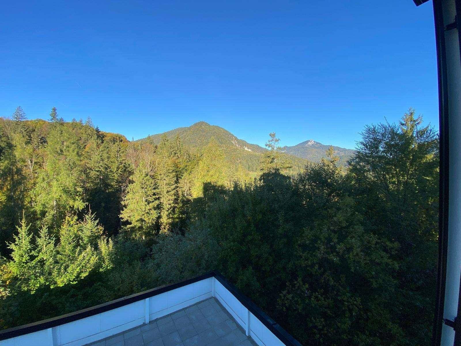 Weitläufiger Blick von einem Balkon auf bewaldete Berge und eine grüne Landschaft unter blauem Himmel.