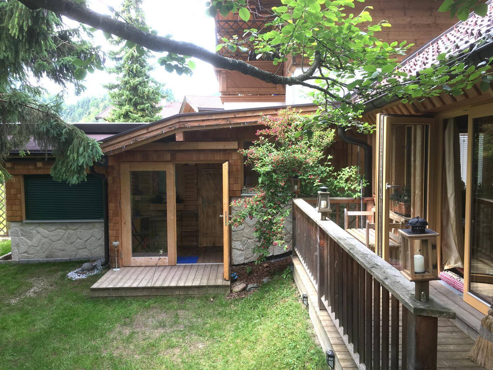 Außenansicht des Holzhauses mit Anbau, Holzterrasse und gepflegtem Gartenbereich.