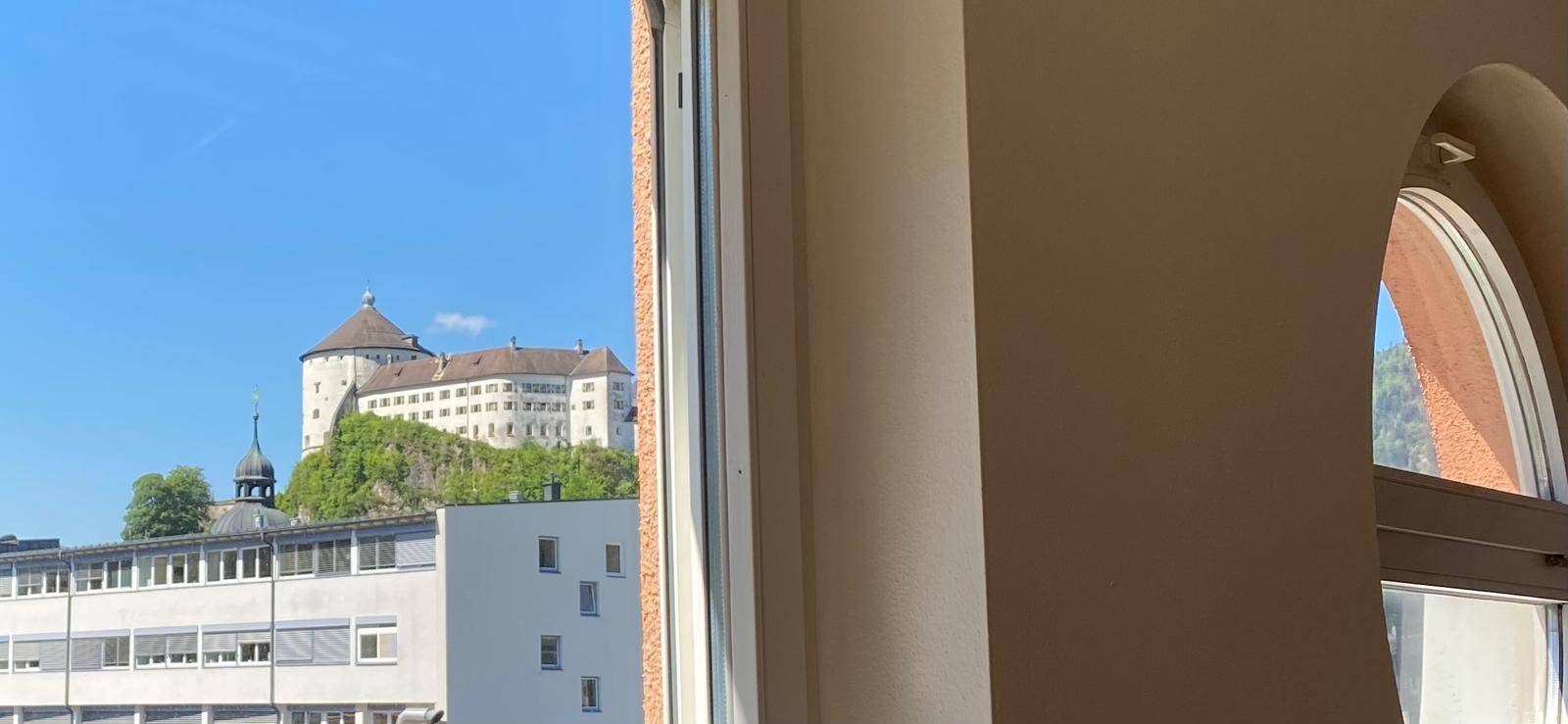 Ausblick aus einem Fenster auf eine imposante Burg auf einem Hügel und umliegende Gebäude.