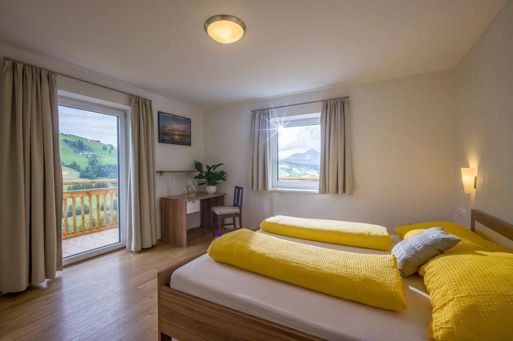 Schlafzimmer mit Doppelbett, Schreibtisch und Balkonzugang, bietet einen weiten Blick auf die Landschaft.