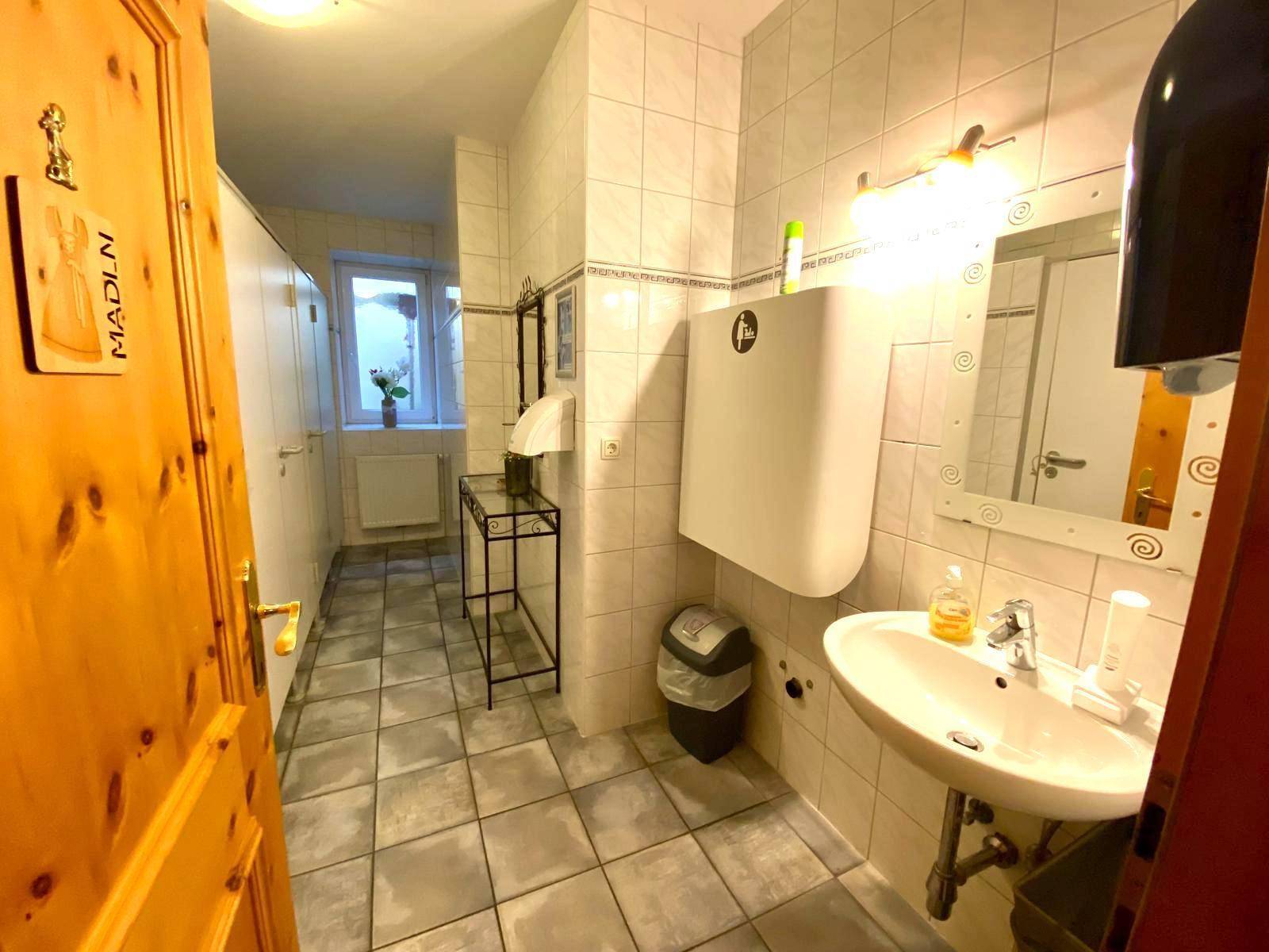 Helles Badezimmer mit Fliesenboden, Waschbecken, Spiegel und Fenster, ausgestattet mit Wickeltisch.