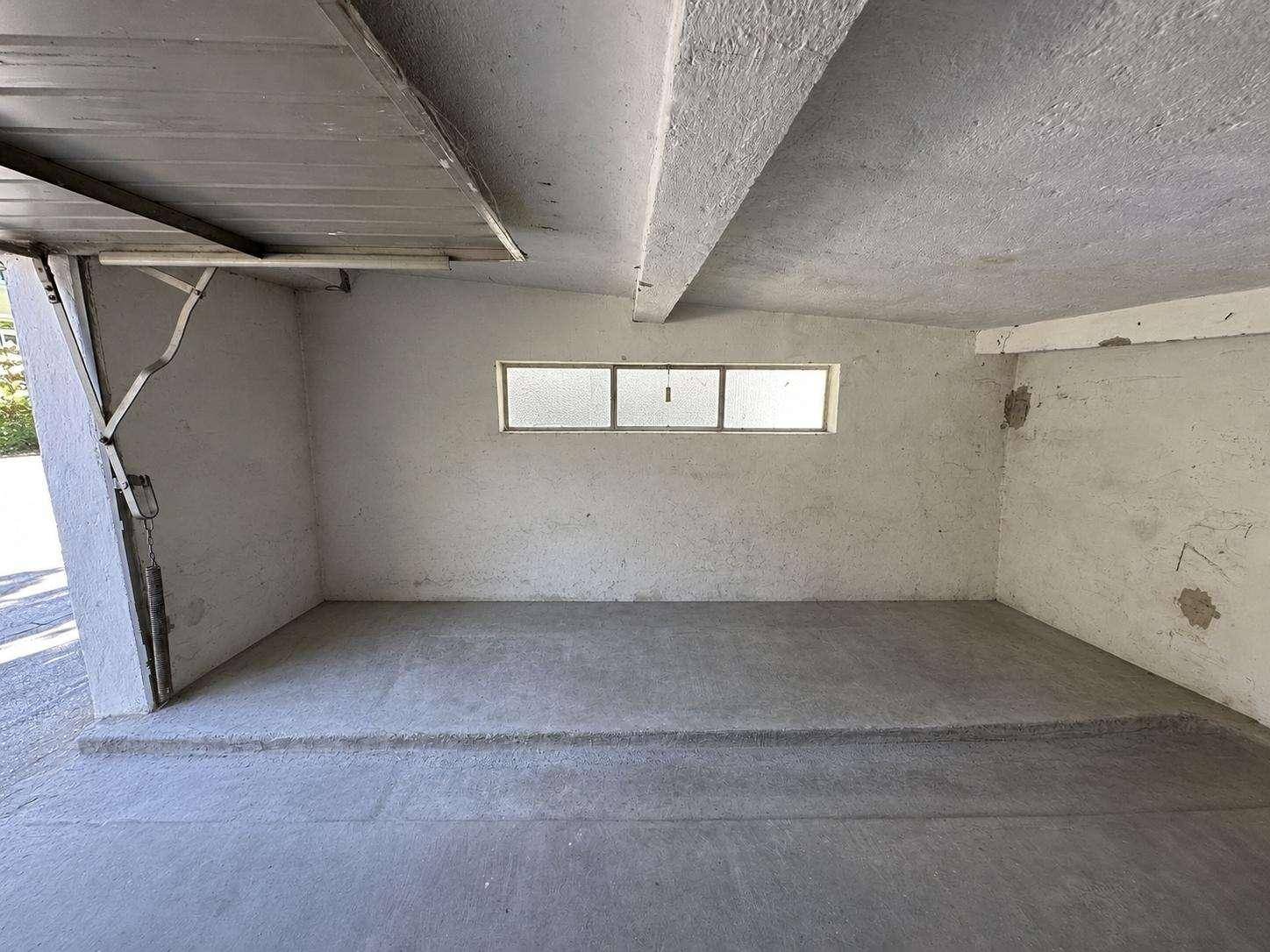 Innenansicht einer leeren Garage mit Betonboden, Wänden und einem kleinen Fenster.