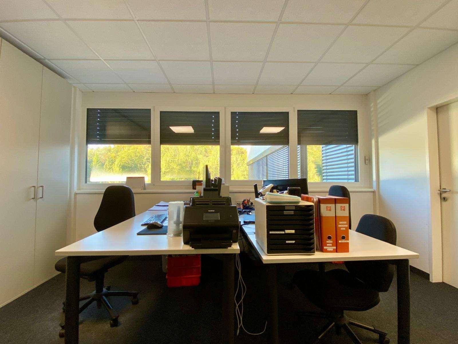 Heller Büroraum mit einem Schreibtisch, Büroausstattung und großen Fenstern, die viel Tageslicht hereinlassen.