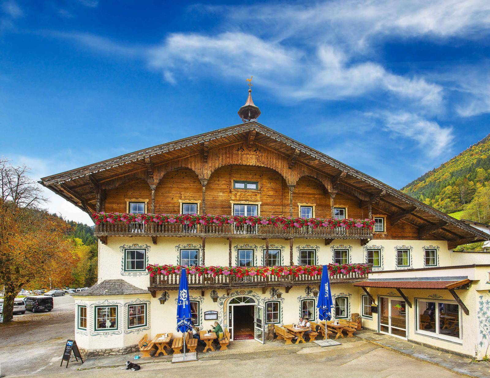Traditionelles Gasthaus mit reich verzierten Holzbalkonen und blühenden Blumenkästen in alpiner Landschaft.