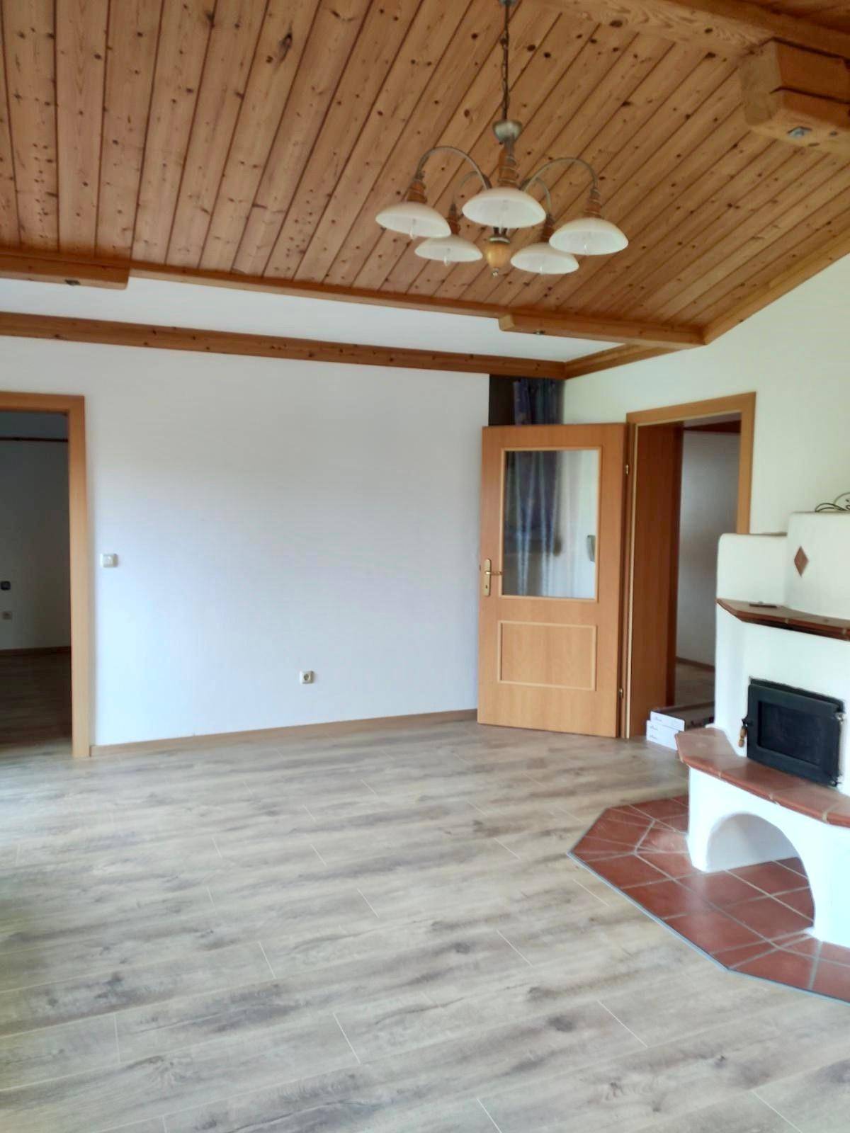Helles Wohnzimmer mit Holzbalkendecke, neuem Laminatboden und Kaminofen.