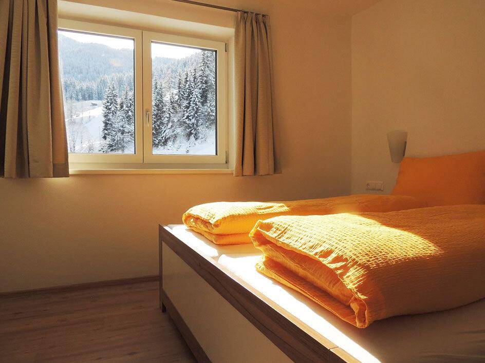 Helles Schlafzimmer mit Doppelbett und Blick auf die verschneite Winterlandschaft durch das Fenster.