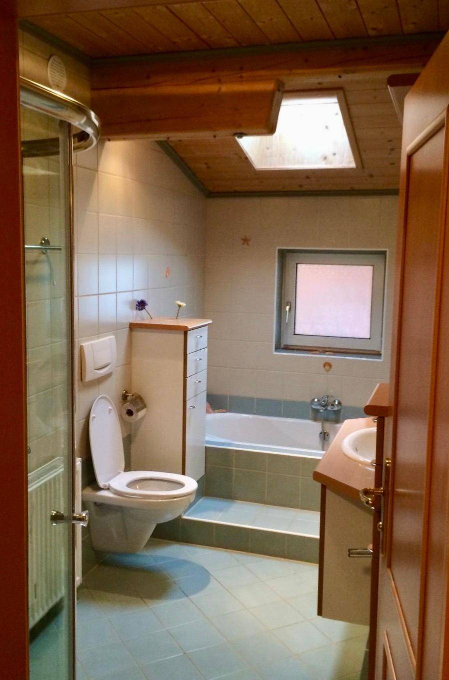 Badezimmer mit Badewanne, Dusche, WC und Dachfenster für natürliche Belüftung.