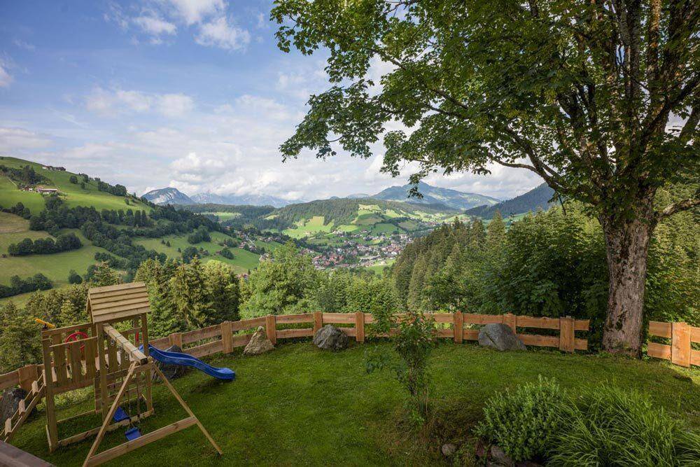 Grüner Gartenbereich mit Kinderspielplatz und Holzzaun, eingebettet in die idyllische Berglandschaft.