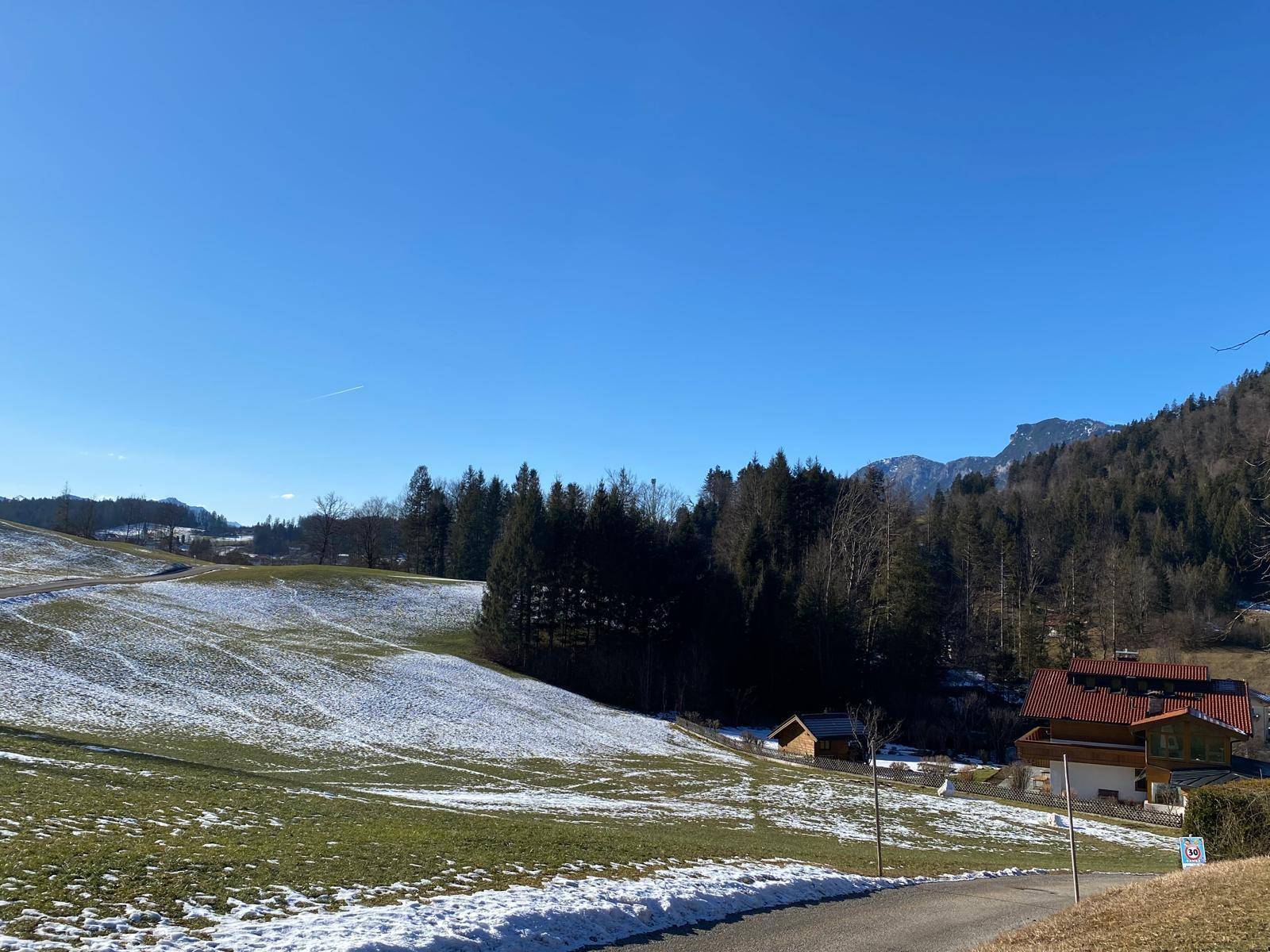 Winterliche Landschaft mit schneebedeckten Feldern, dunklen Wäldern und Bergen unter klarem Himmel.