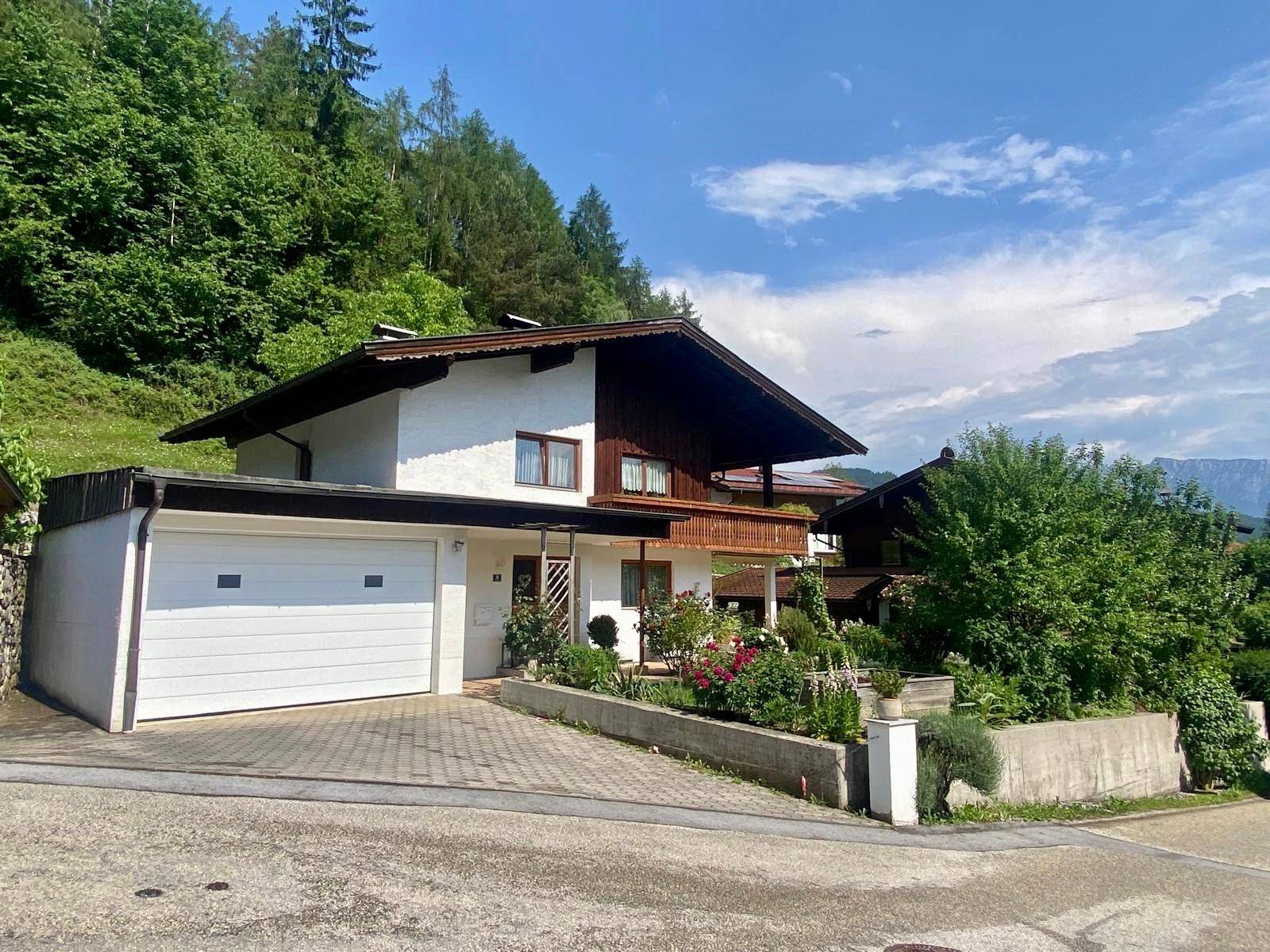 Traditionelles Haus mit integrierter Garage und gepflasterter Auffahrt, umgeben von üppigem Grün.