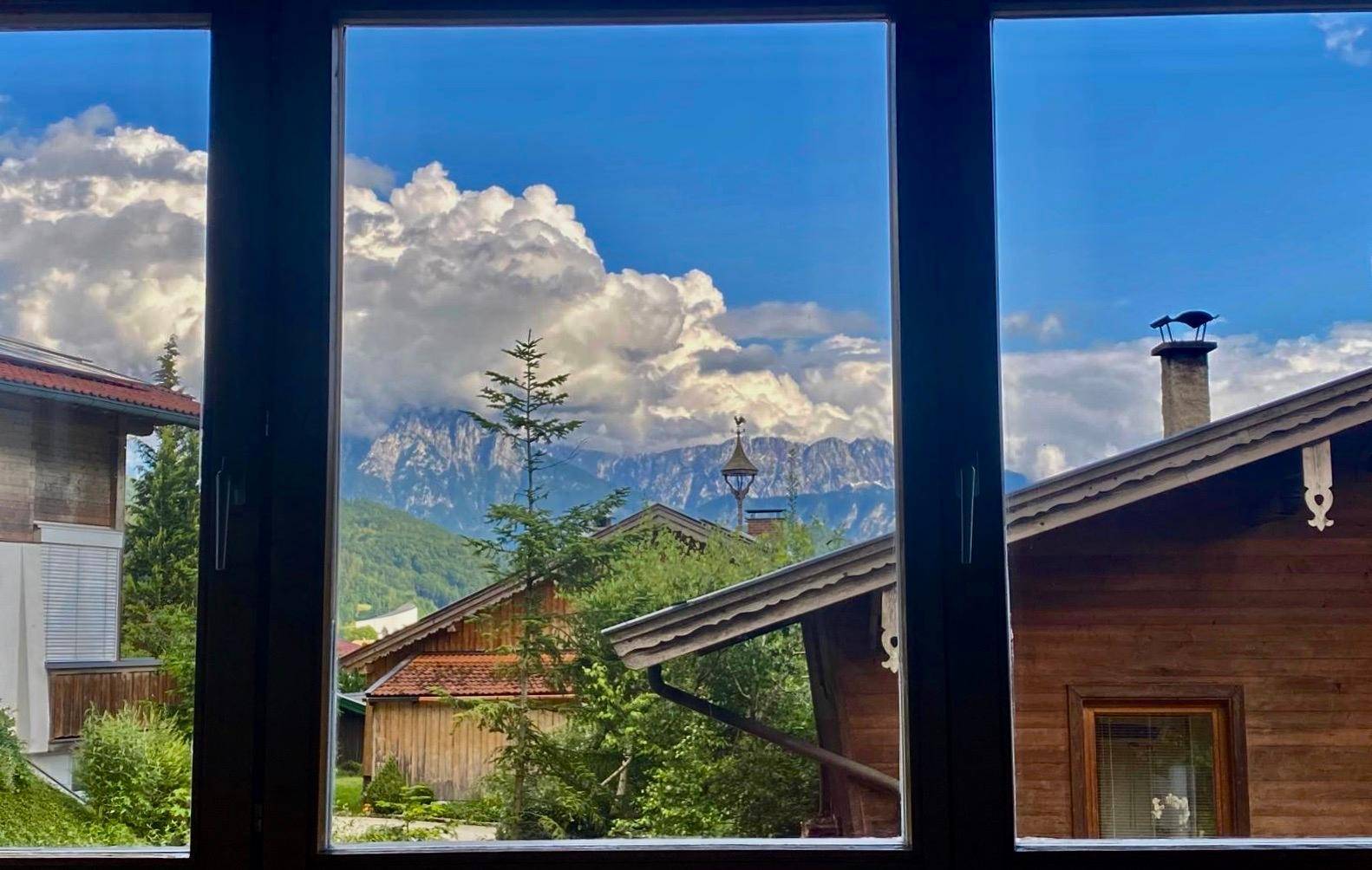 Fensterblick auf die beeindruckende Berglandschaft und die umliegenden Häuser unter blauem Himmel.