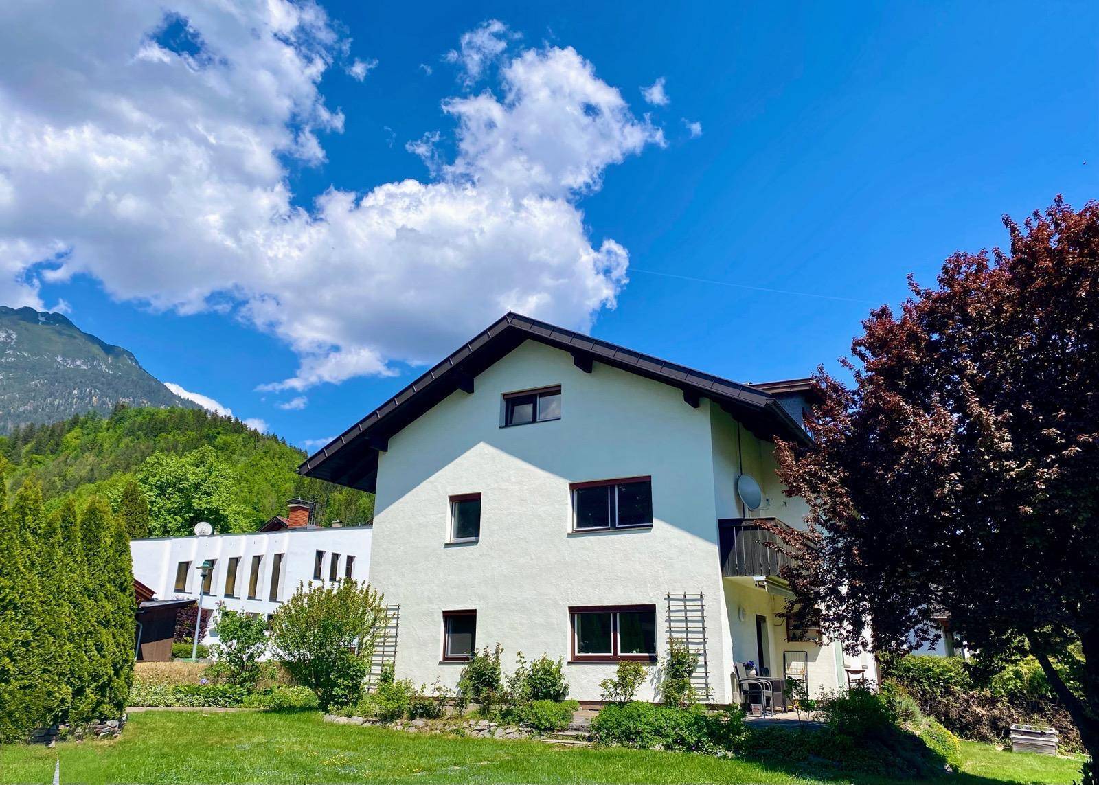 Freistehendes Haus mit großem Garten und Bergblick unter blauem Himmel.