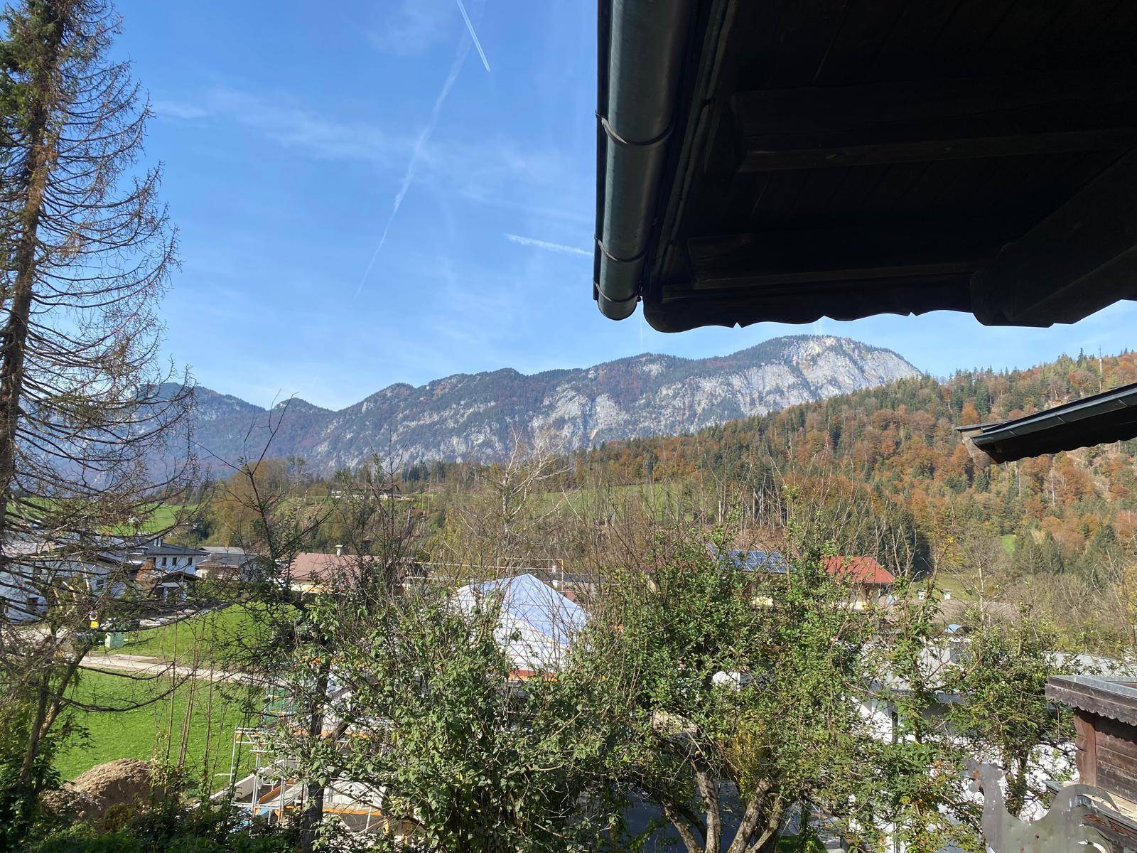 Weitläufiger Blick auf die umliegende Berglandschaft und herbstliche Wälder unter blauem Himmel.