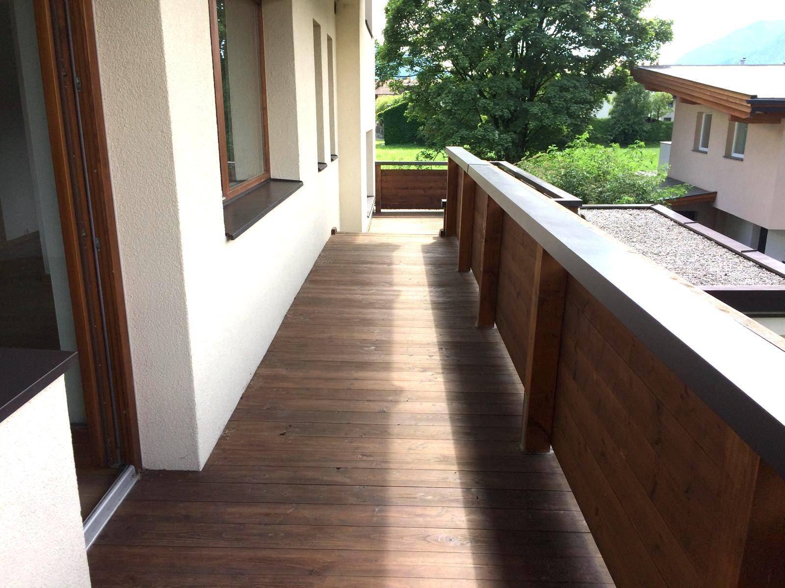 Langer Holzbalkon mit Geländer und Blick auf die grüne Umgebung.