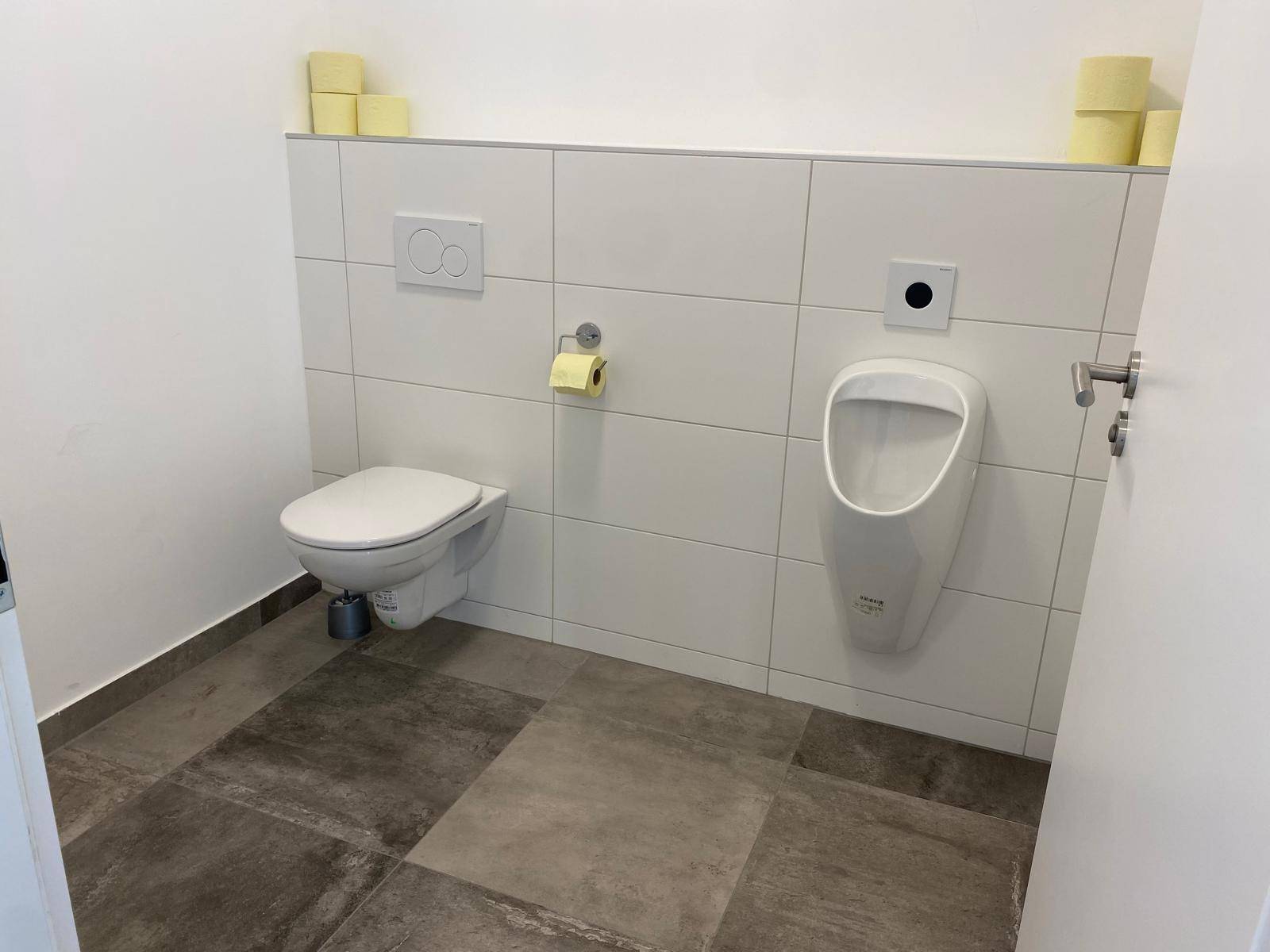 Herren-WC mit wandhängender Toilette, Urinal und modernen Fliesen in Weiß und Grau, sehr gepflegt.