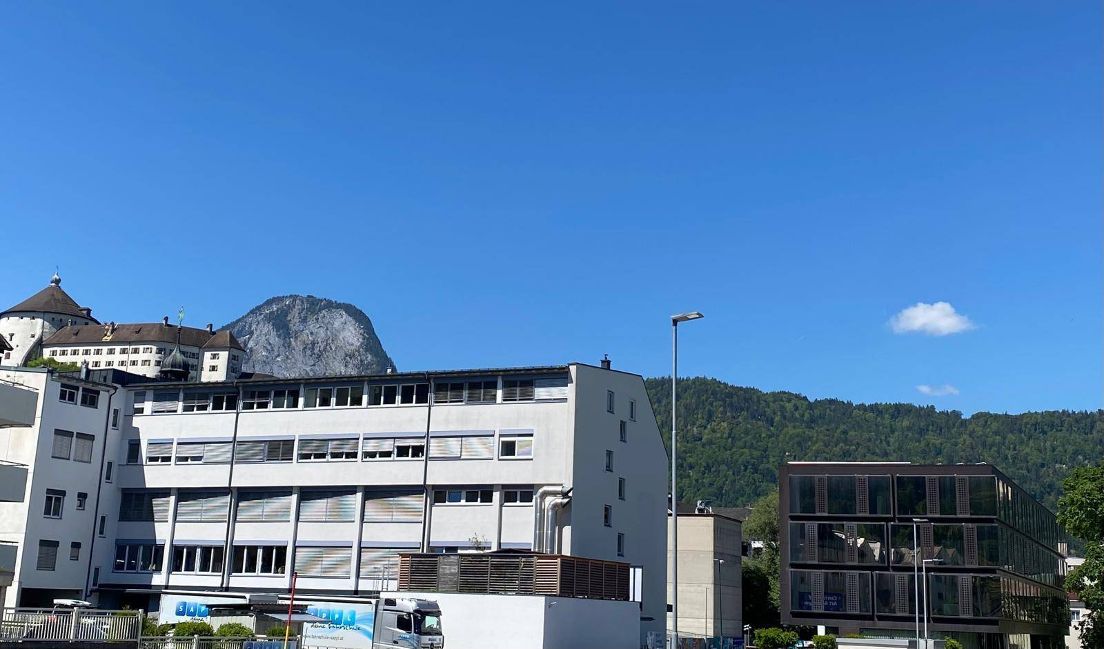 Stadtansicht mit Gebäuden, einem markanten Berg im Hintergrund und einer Burg auf einem Hügel.