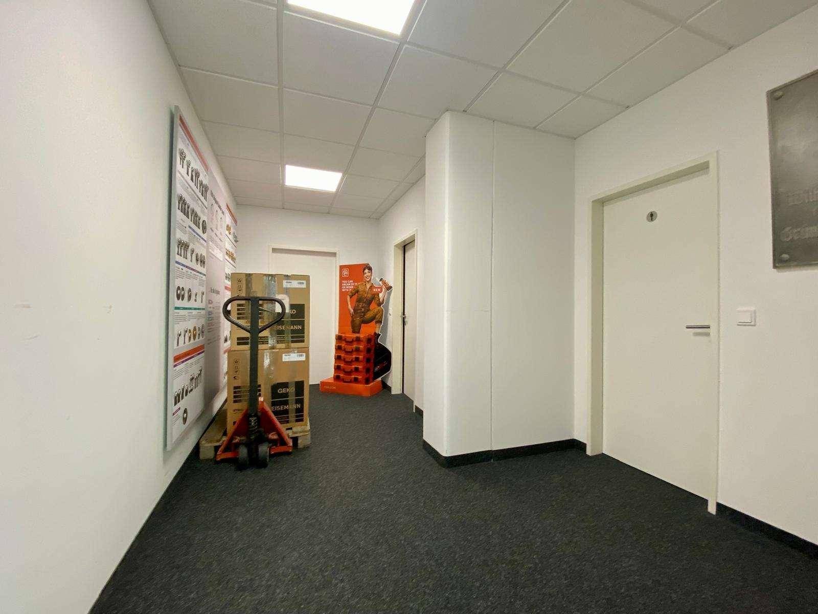 Heller Flur mit weißen Wänden und dunklem Teppichboden, der zu verschiedenen Räumen im Gebäude führt.