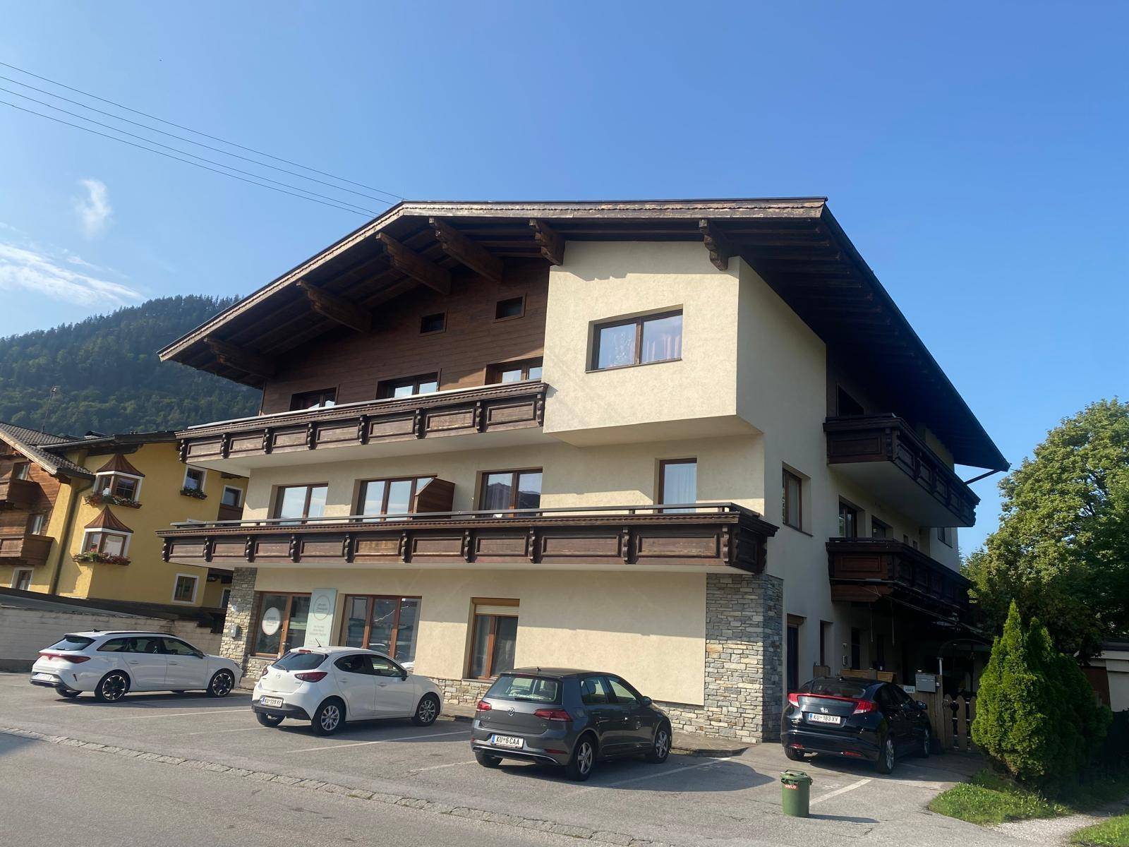 Alpines Wohnhaus mit mehreren Balkonen, Stein- und Holzfassade sowie Parkmöglichkeiten im Freien.