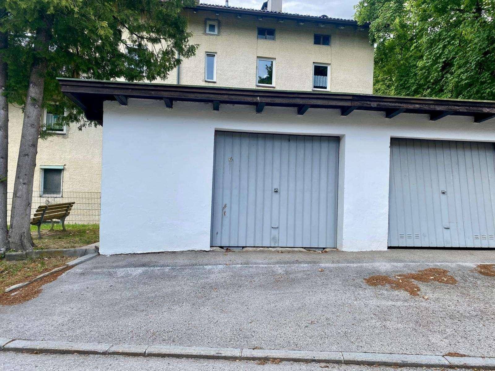 Außenansicht der Garage mit zwei grauen Toren und dem dahinterliegenden Wohngebäude.