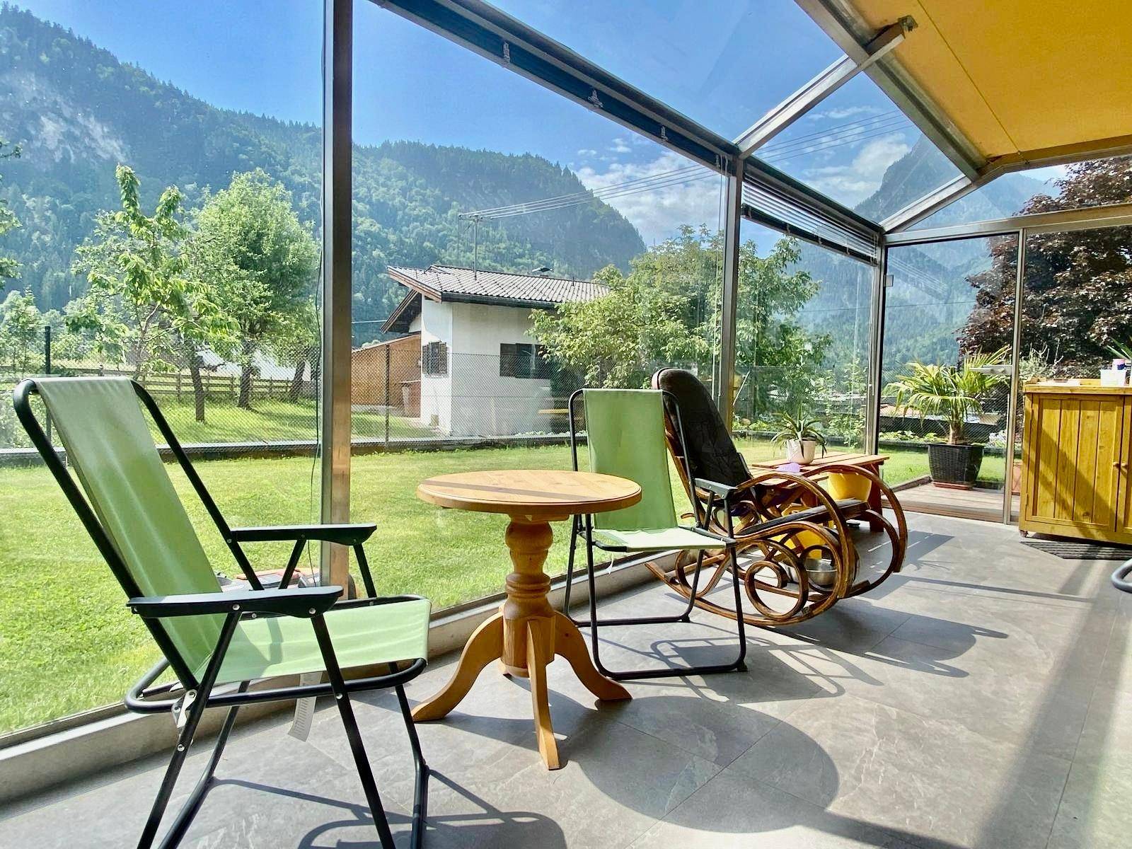 Heller Wintergarten mit Sitzgelegenheiten und Panoramablick auf die umliegende Berglandschaft.