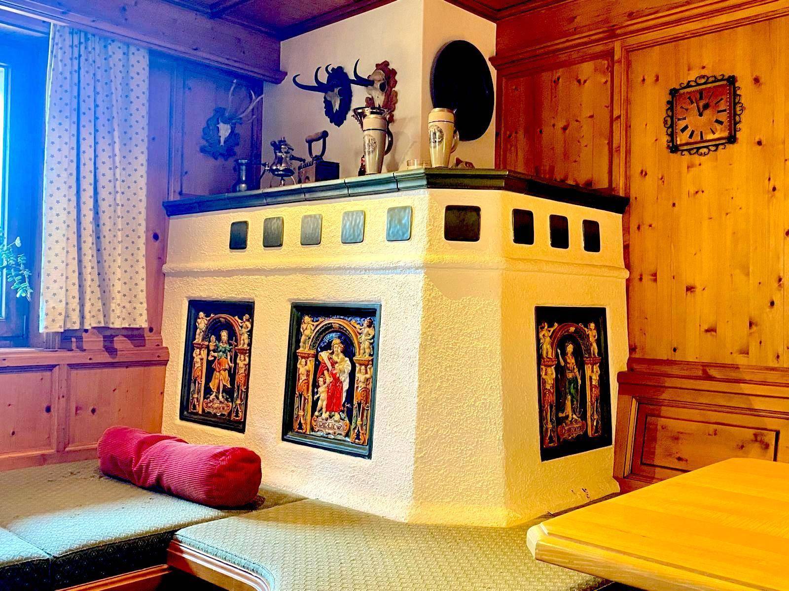 Detailansicht des traditionellen Kachelofens mit kunstvollen Verzierungen im Essbereich.