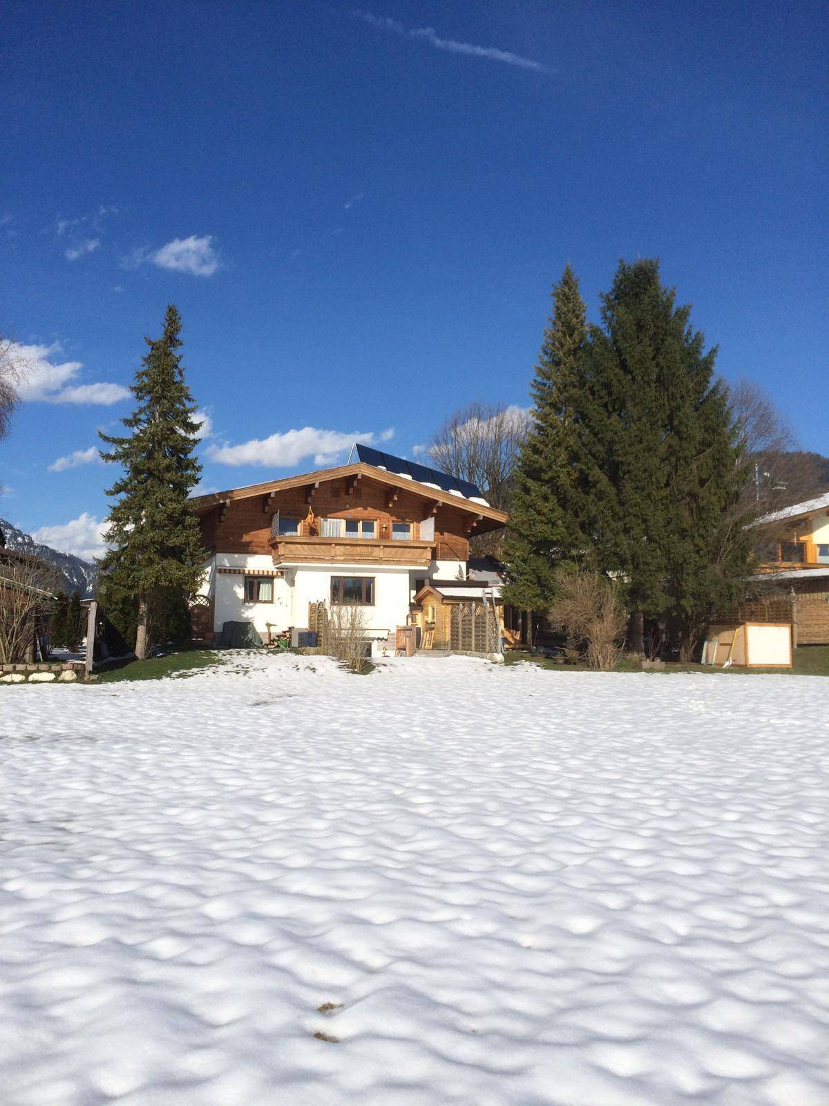 Winterliche Ansicht des Hauses mit verschneitem Garten und blauer Himmel.