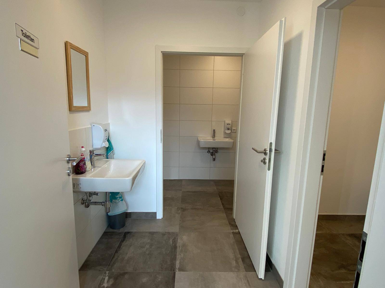 Eingangsbereich zu den Toiletten mit mehreren Waschbecken und modernen Fliesen, hell und gepflegt.
