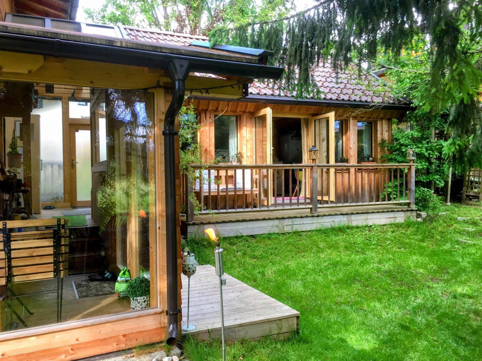 Charmantes Holzhaus mit Terrasse und grünem Rasen, umgeben von Bäumen im Garten.