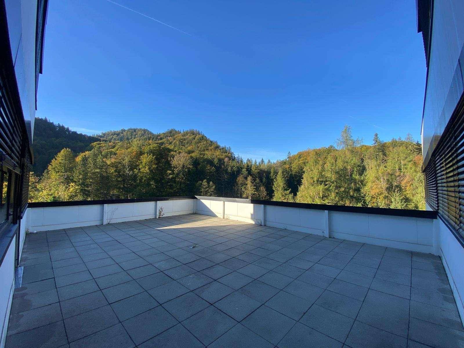 Weitläufige Terrasse mit Panoramablick auf die umliegende Berglandschaft und dichte Wälder unter blauem Himmel.