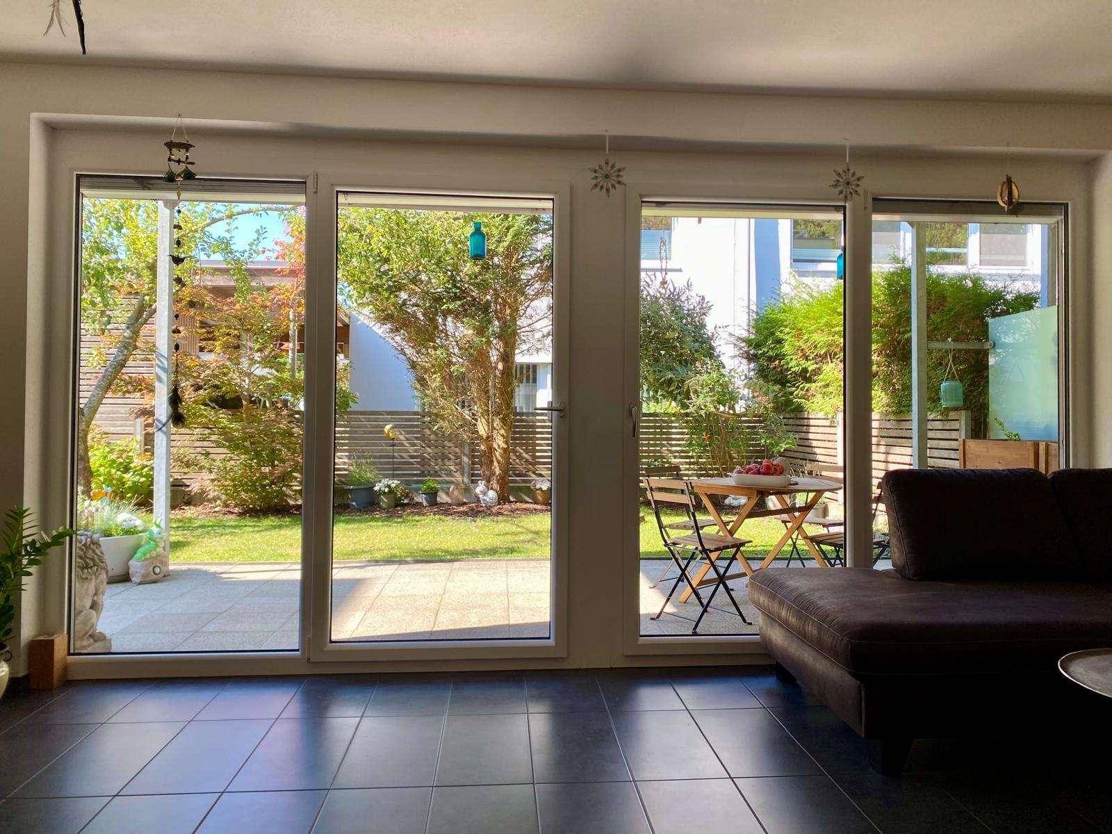 Wohnzimmer mit dunklen Fliesen und großen Schiebetüren, die zum privaten Garten mit Terrasse führen.