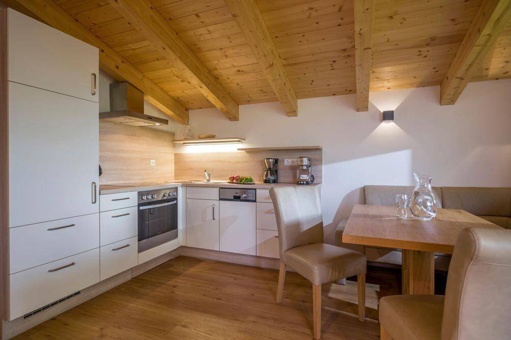 Moderne Einbauküche mit hellen Fronten, Holzarbeitsplatte und Essbereich unter Holzbalkendecke.